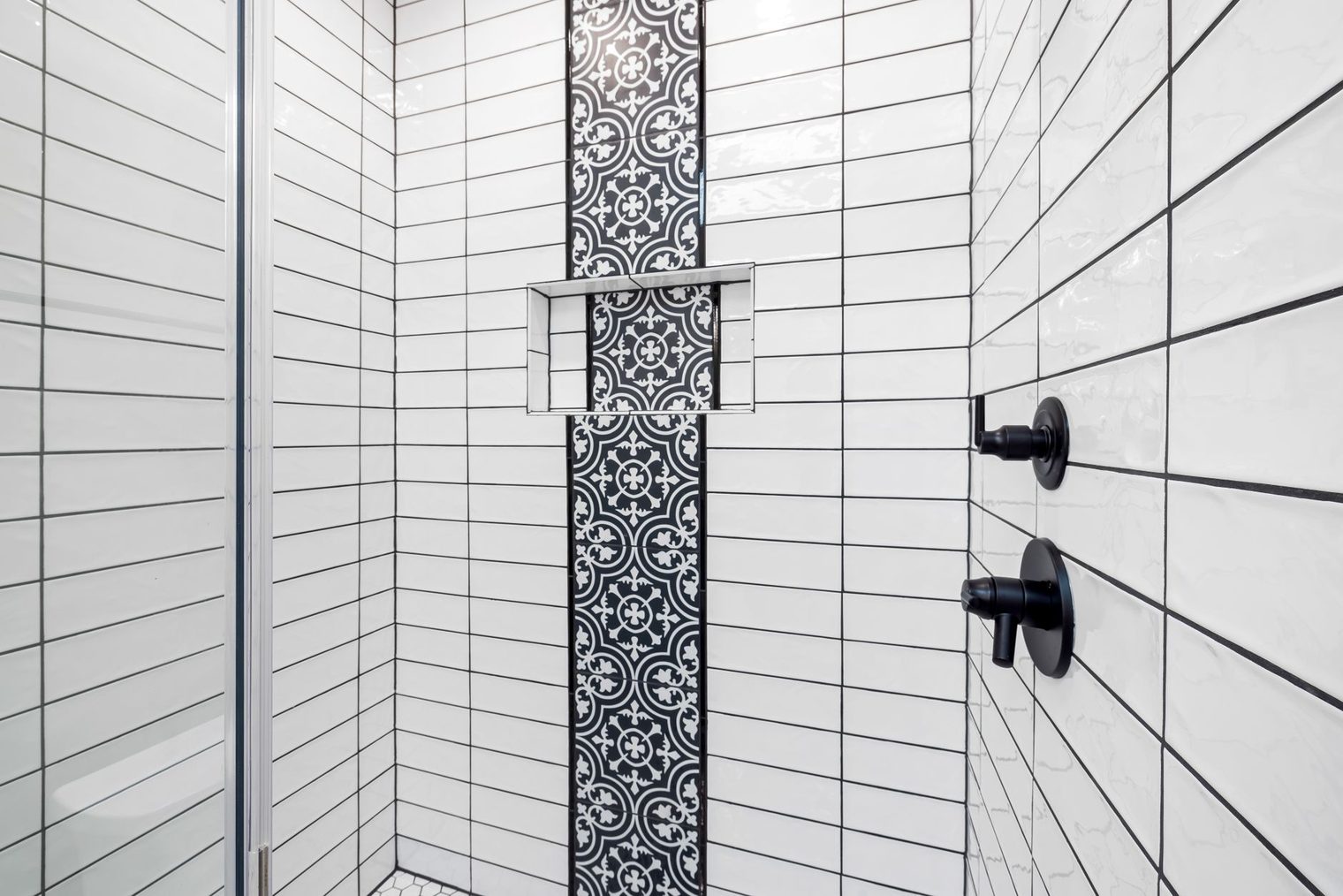 Tiled shower wall in white subway tile with a patterned accent stripe and a built-in niche