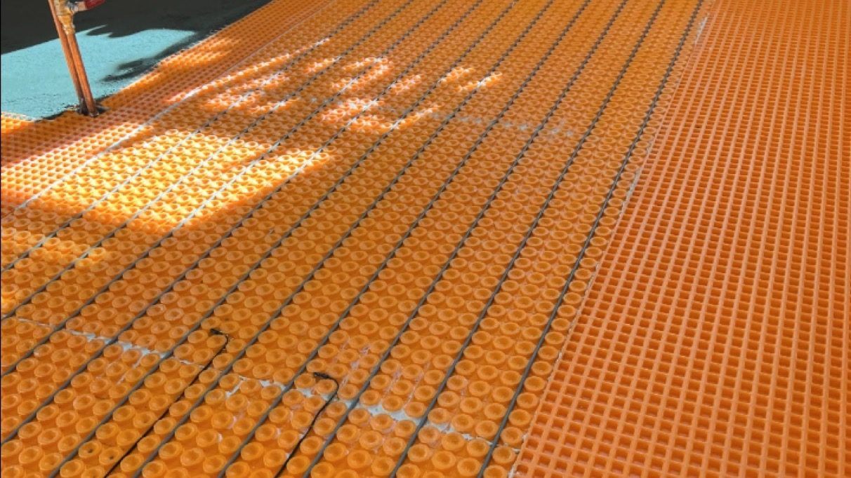 Orange DITRA-Heat uncoupling membrane with electric floor heating cable run across a floor before tiling