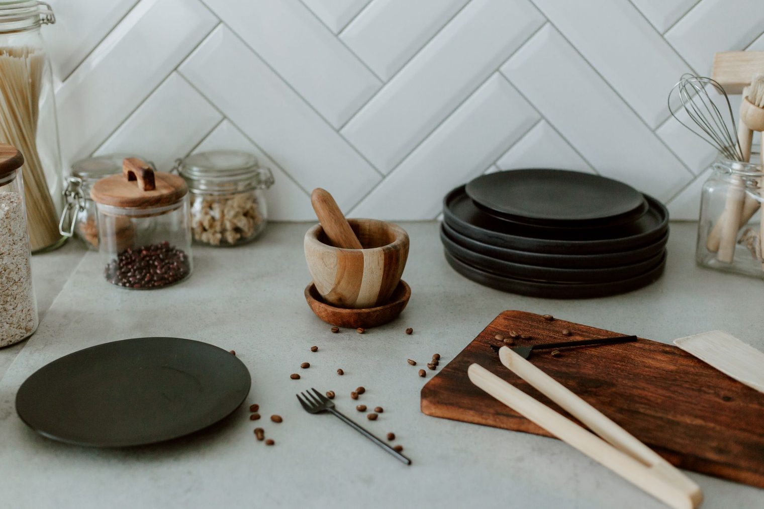 White herringbone tile backsplash behind a kitchen countertop with jars and plates