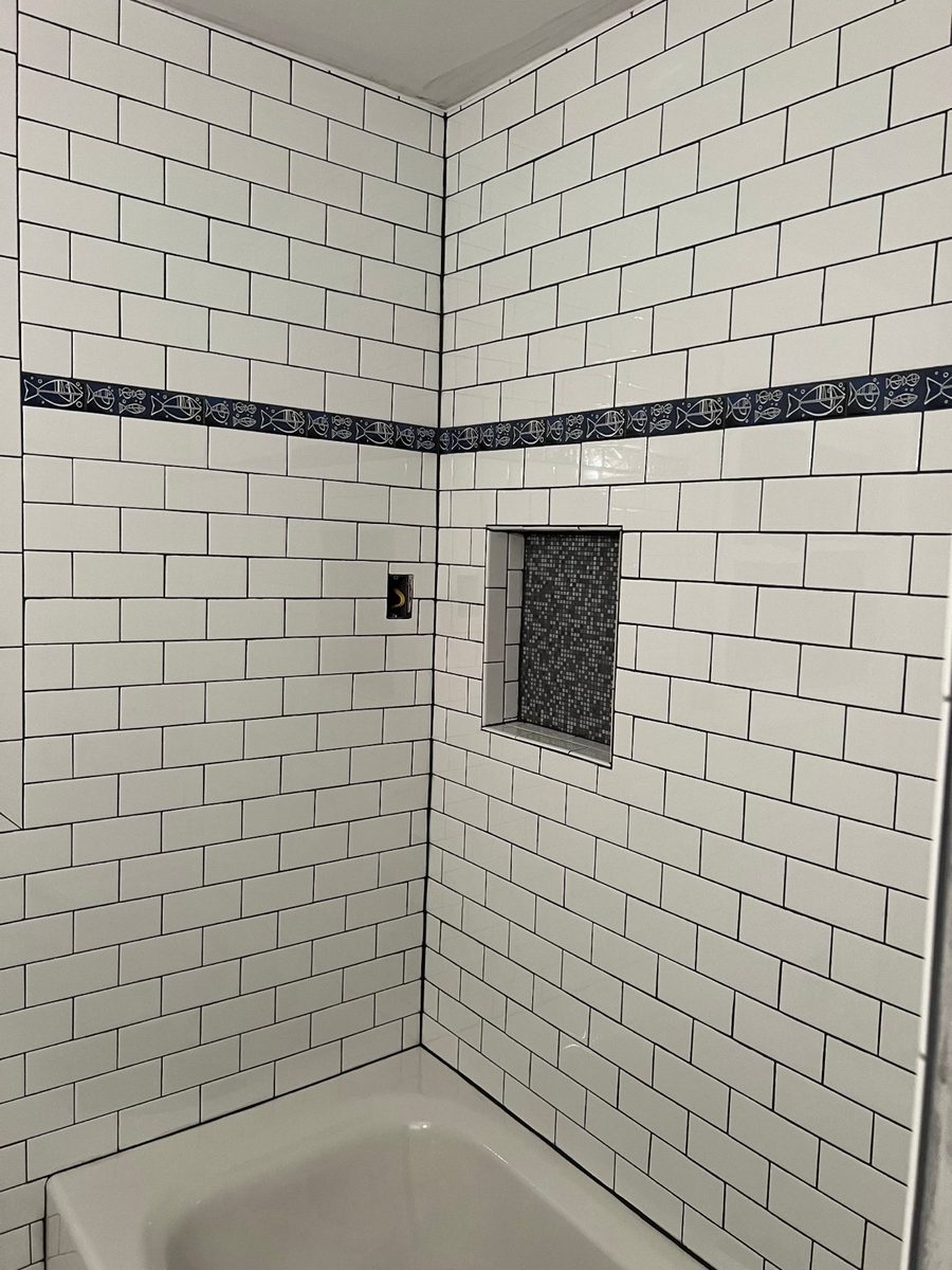 White subway tile bathtub surround with a mosaic accent band by MCode