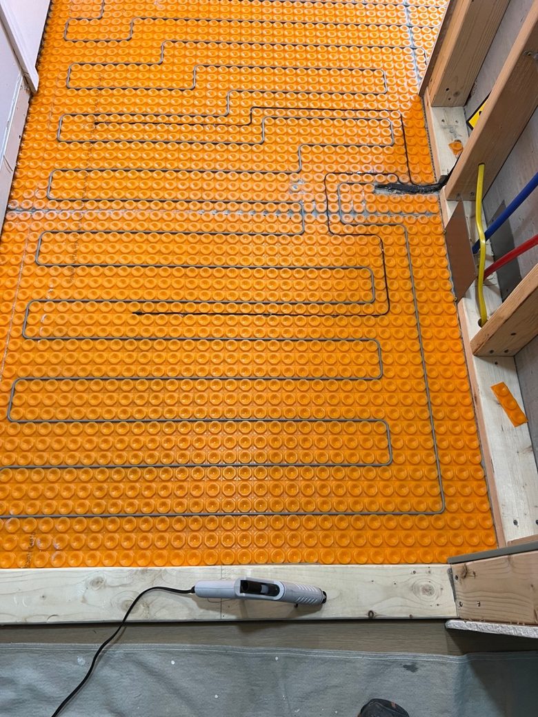 Electric radiant floor heating cable snaked into the studs of an uncoupling membrane before tile