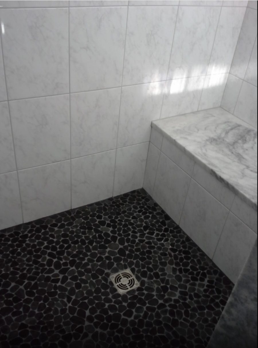 Natural marble shower with a black pebble stone floor and marble bench, all sealed