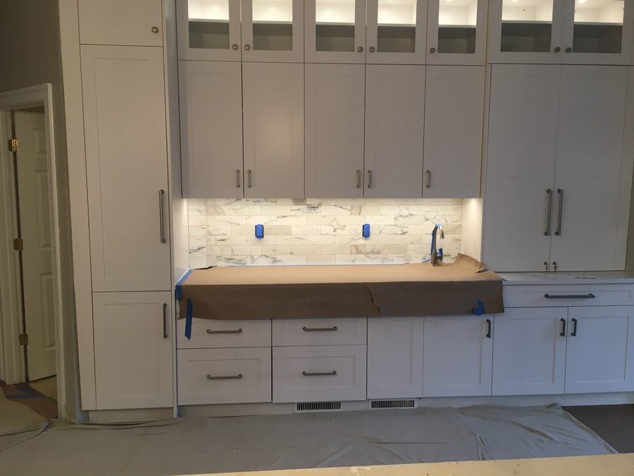 Calacatta marble subway tile stone backsplash with soft grey veining behind glass-front cabinets