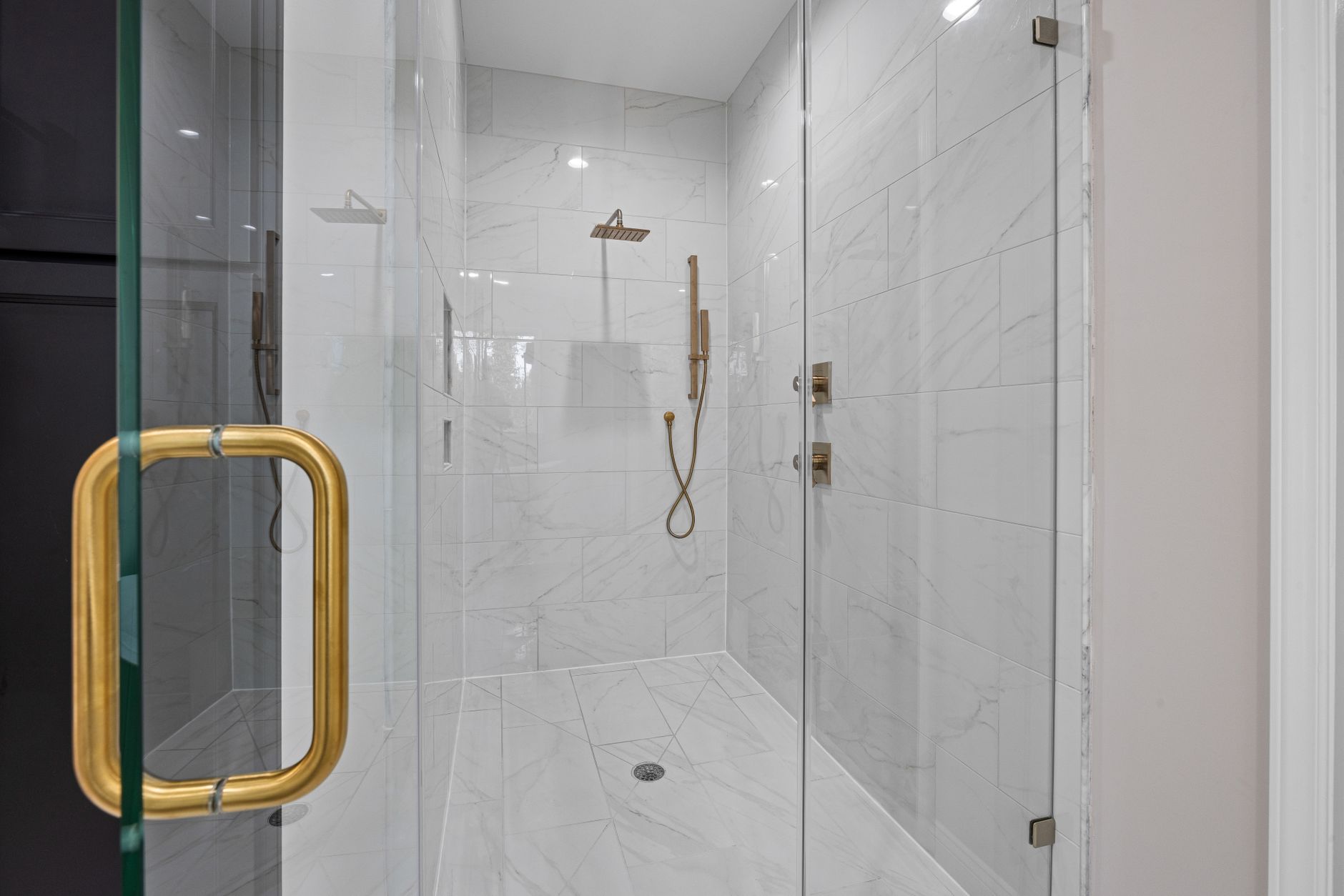 Walk-in shower tiled in large format marble-look porcelain with a glass door and brass fixtures