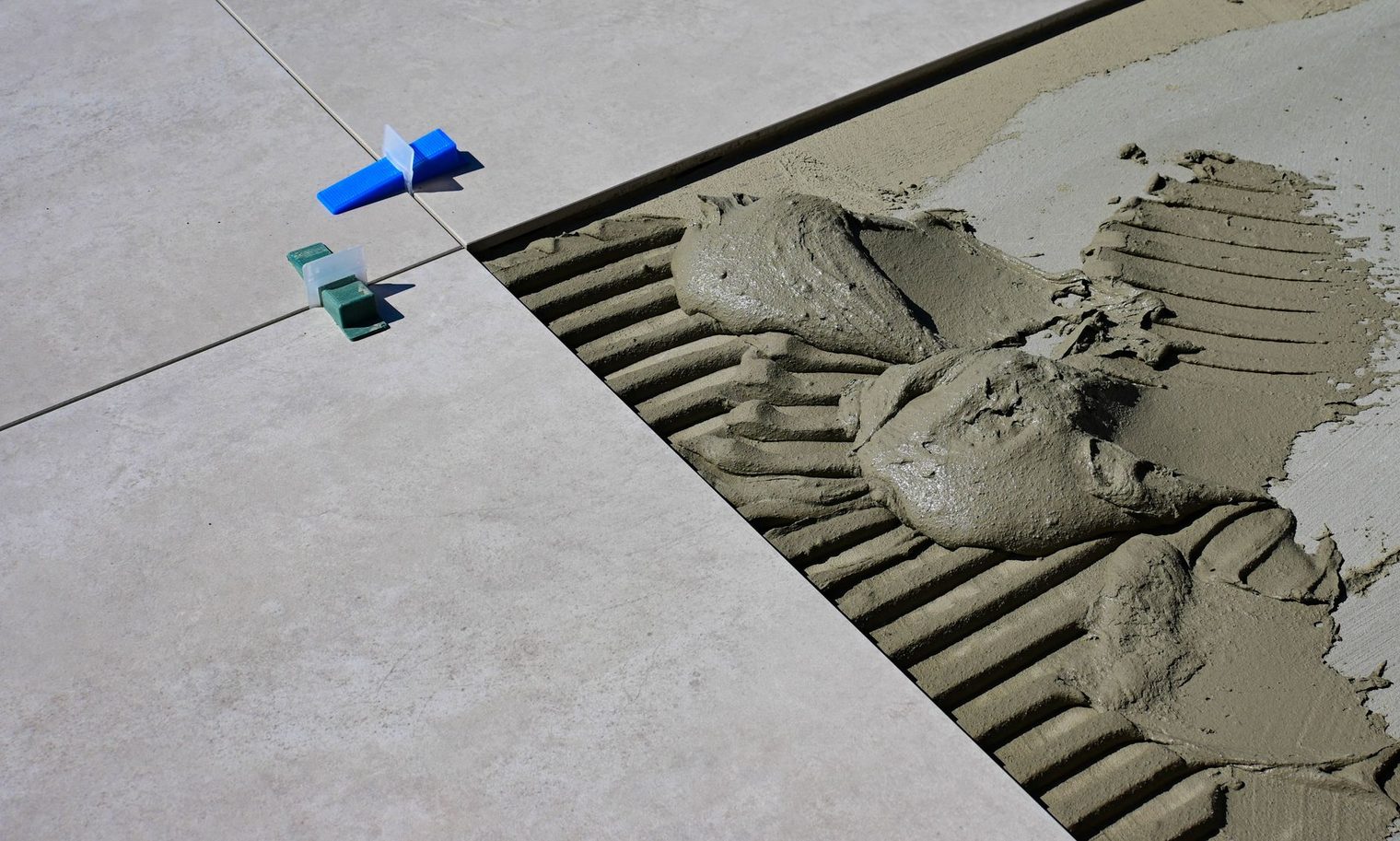 Large format floor tile being set in notched thinset with leveling clips to stop lippage