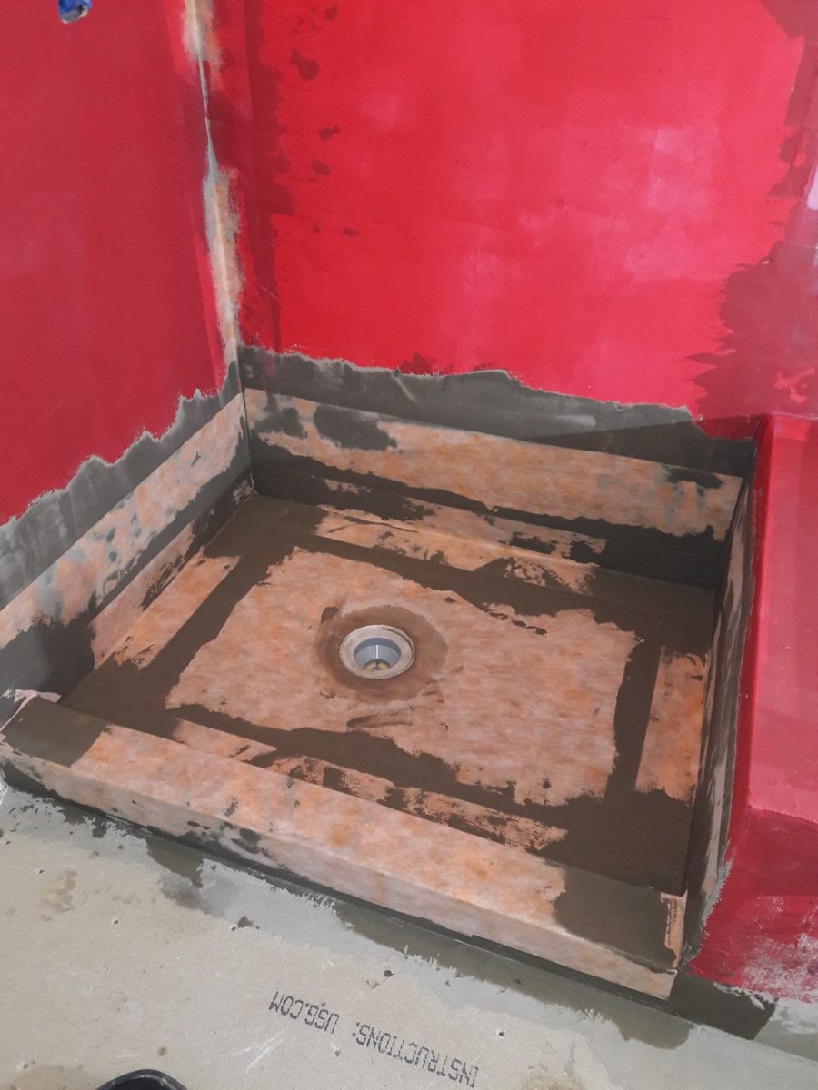 Shower pan waterproofed with a bonded membrane over the sloped base before any tile shower pan work
