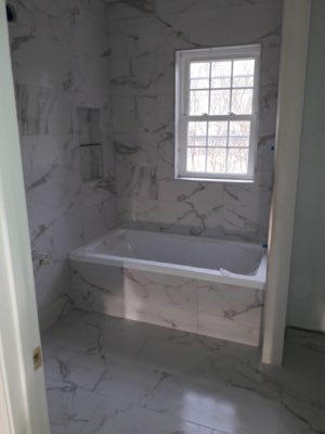 Full marble tile bathroom with tub surround and window