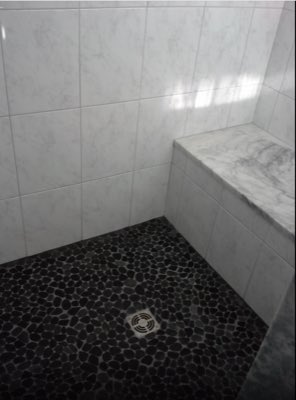 Marble tile shower with black pebble stone floor and marble bench